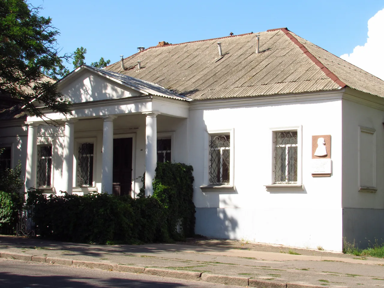 Літній вигляд будинку Дерибаса в Миколаєві з колонадою входу, повним головним фасадом і меморіальною дошкою.