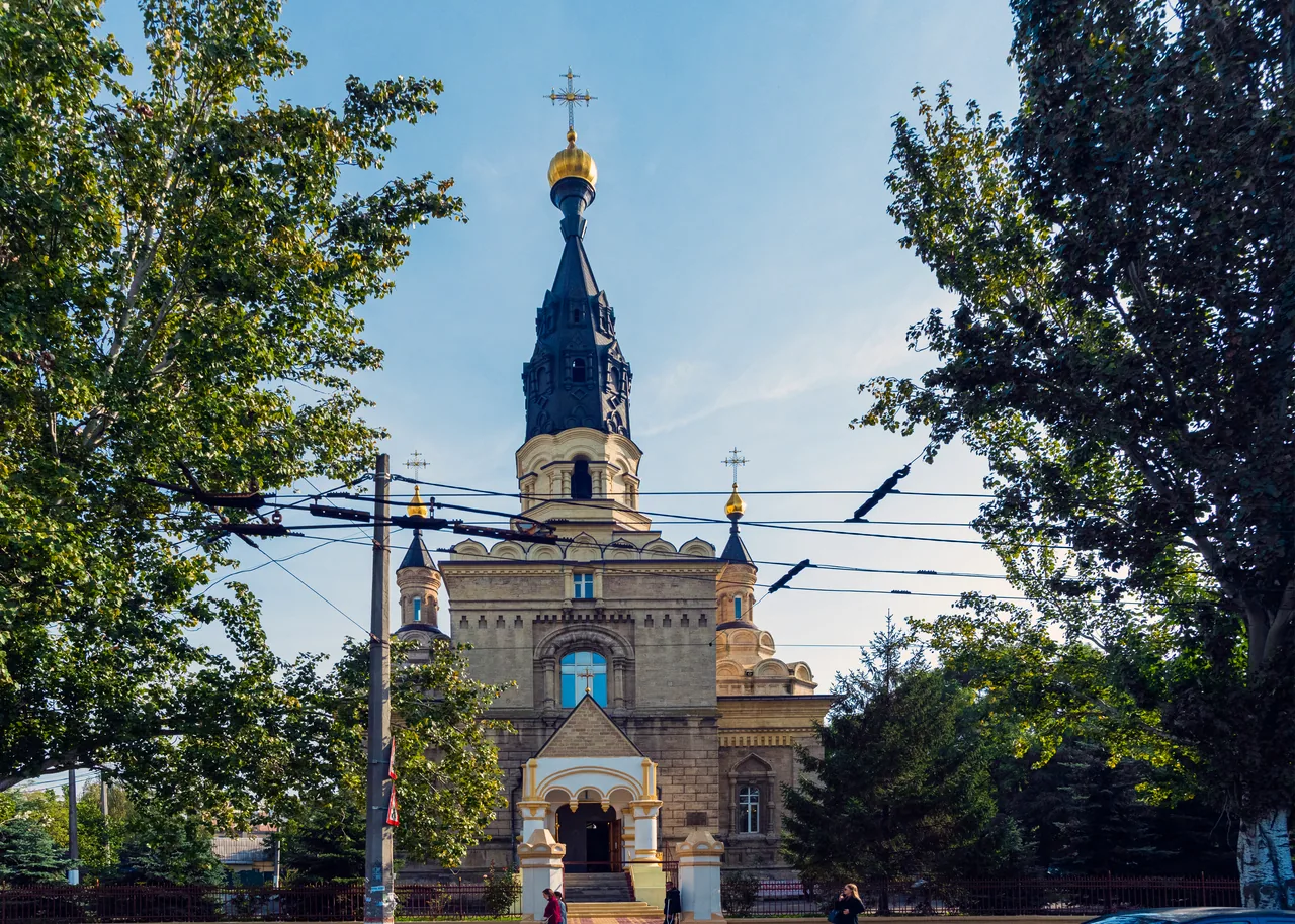 Архівний вигляд головного фасаду Касперівського кафедрального собору в Миколаєві з дзвіницею, входом і зеленими деревами обабіч.