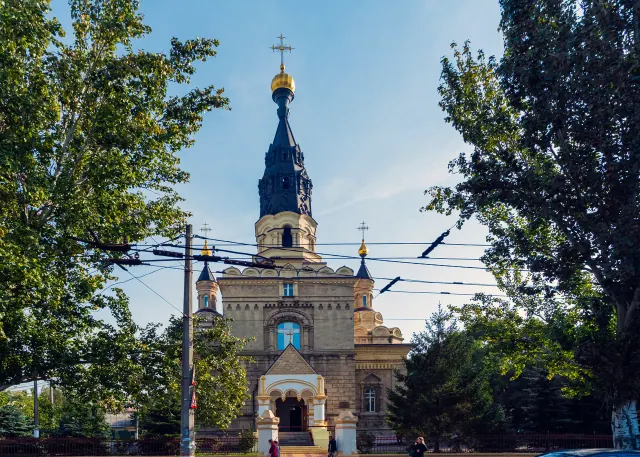 Архівний вигляд головного фасаду Касперівського кафедрального собору в Миколаєві з дзвіницею, входом і зеленими деревами обабіч.